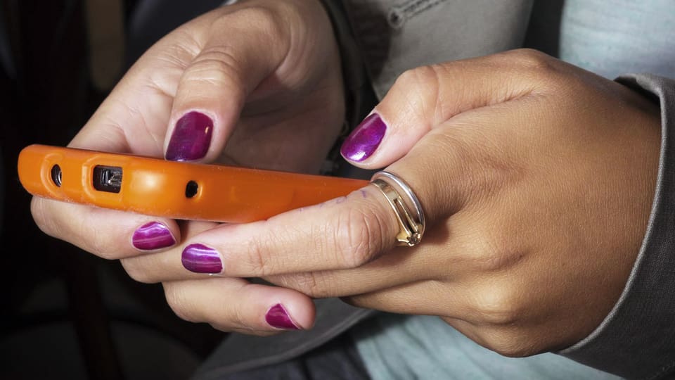 Frau hält ein Smartphone mit oranger Schutzhülle in den Händen und tippt darauf mit dem Daumen.