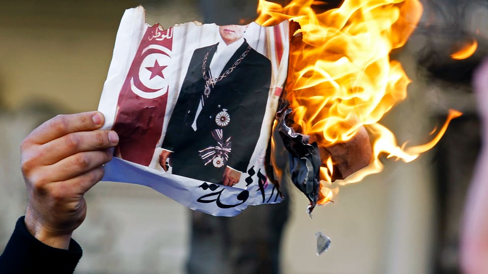Proteste gegen den tunesischen Machthaber Ben Ali 2011 in Frankreich. Ein Mann hält ein brennendes Bild Ben Alis in der Hand. 