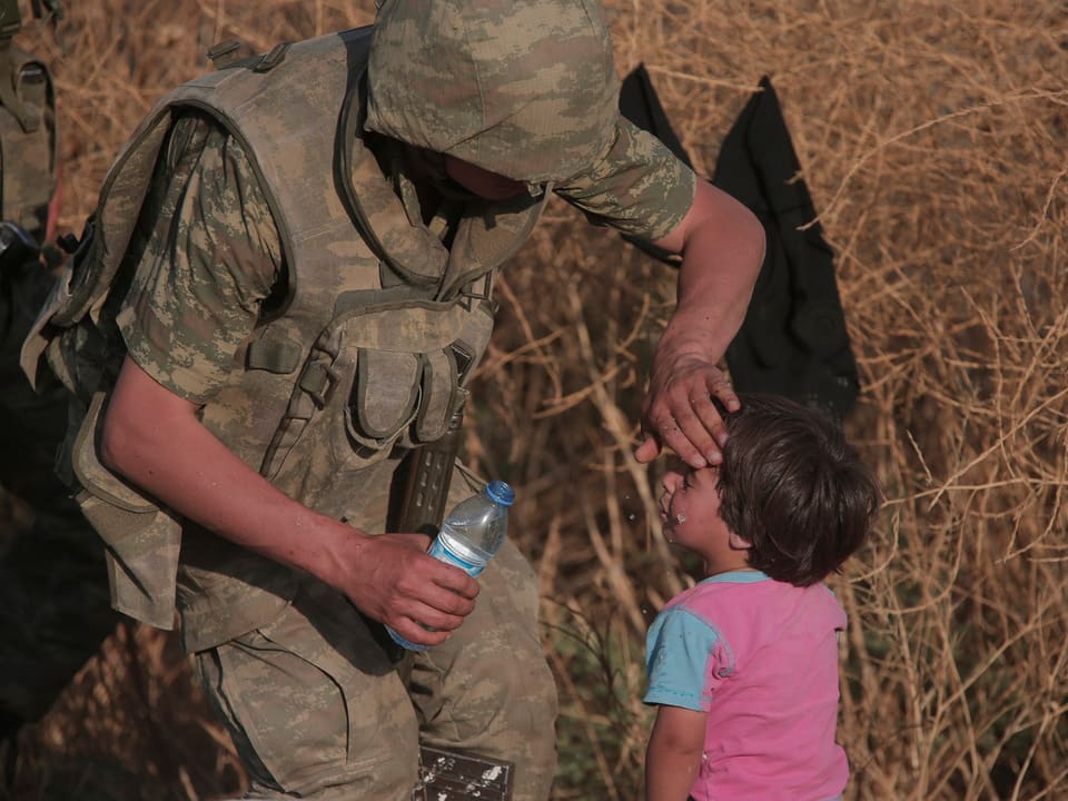 Ein türkischer Soldat verpflegt ein durstiges syrisches Kind.