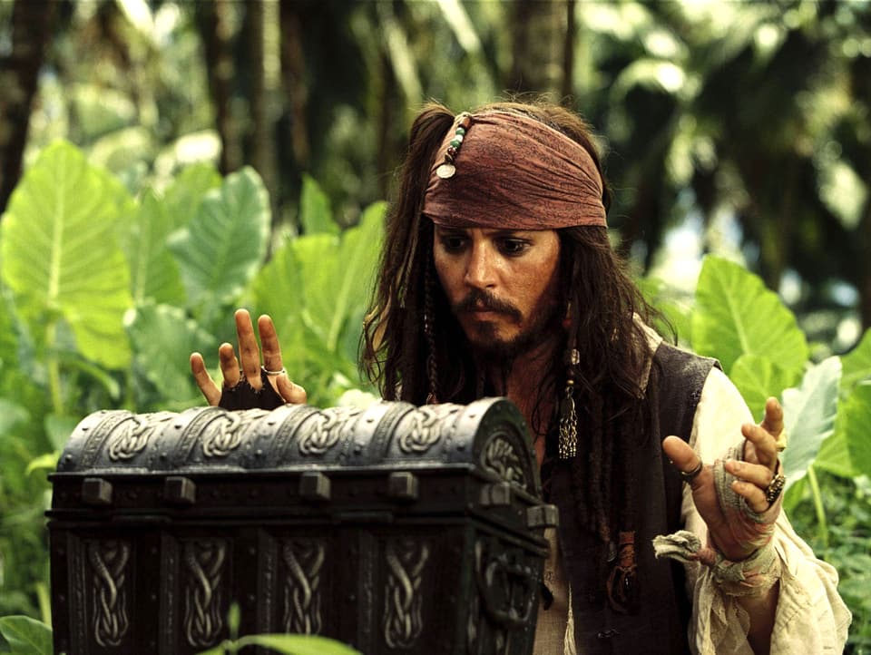 Mann im Piratenkostüm steht gebannt im Dschungel vor einer Schatztruhe