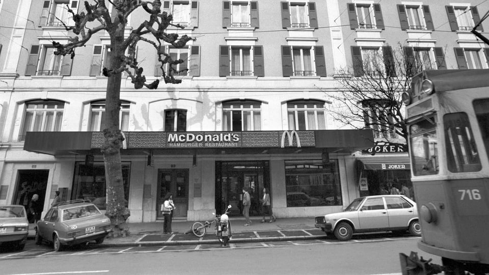 eine schwarz-weiss Aufnahme eines McDonalds in Genf, an der Strasse davor fährt ein Tram