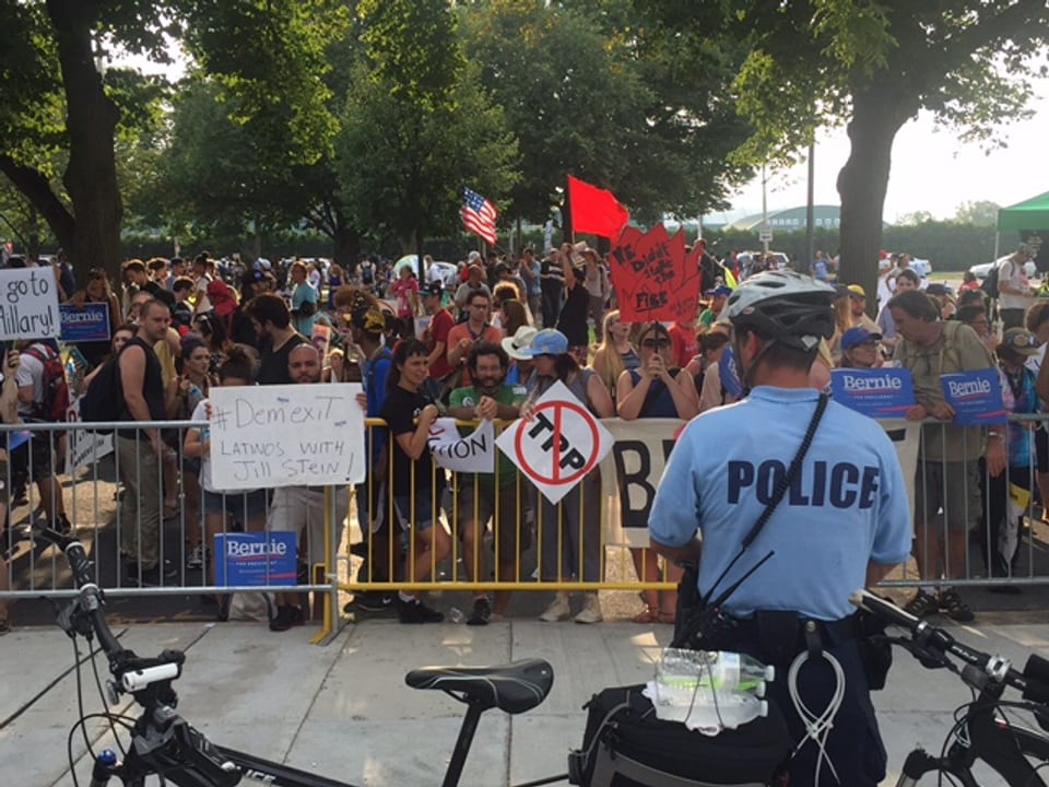 Wütende Demonstranten am Parteitag der Demokraten in Philadelphia vor einem Absperrgitter. Davor steht ein Polizist.