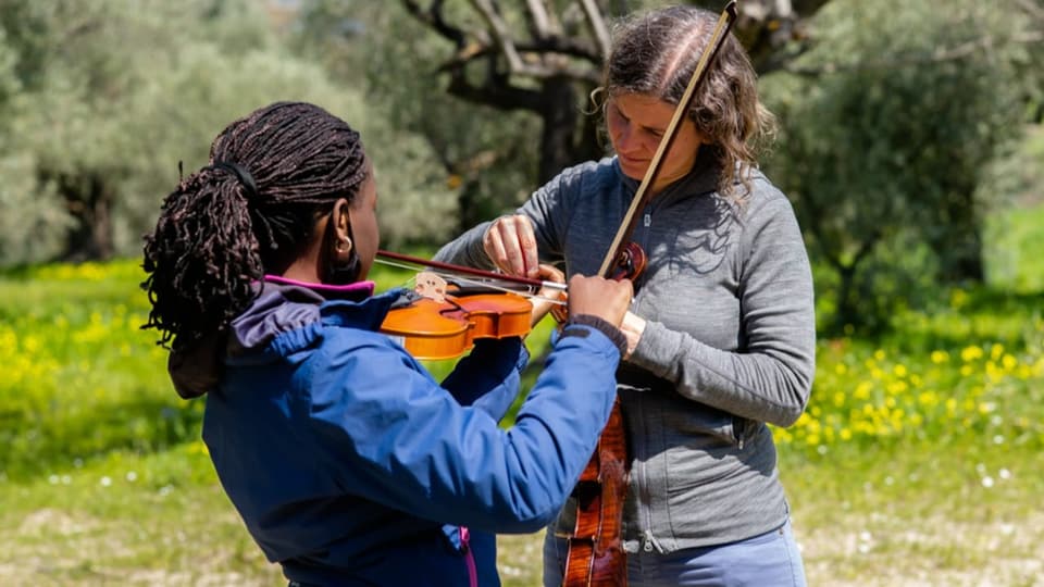 Eine Frau zeigt einem Kind, wie man Geige spielt.