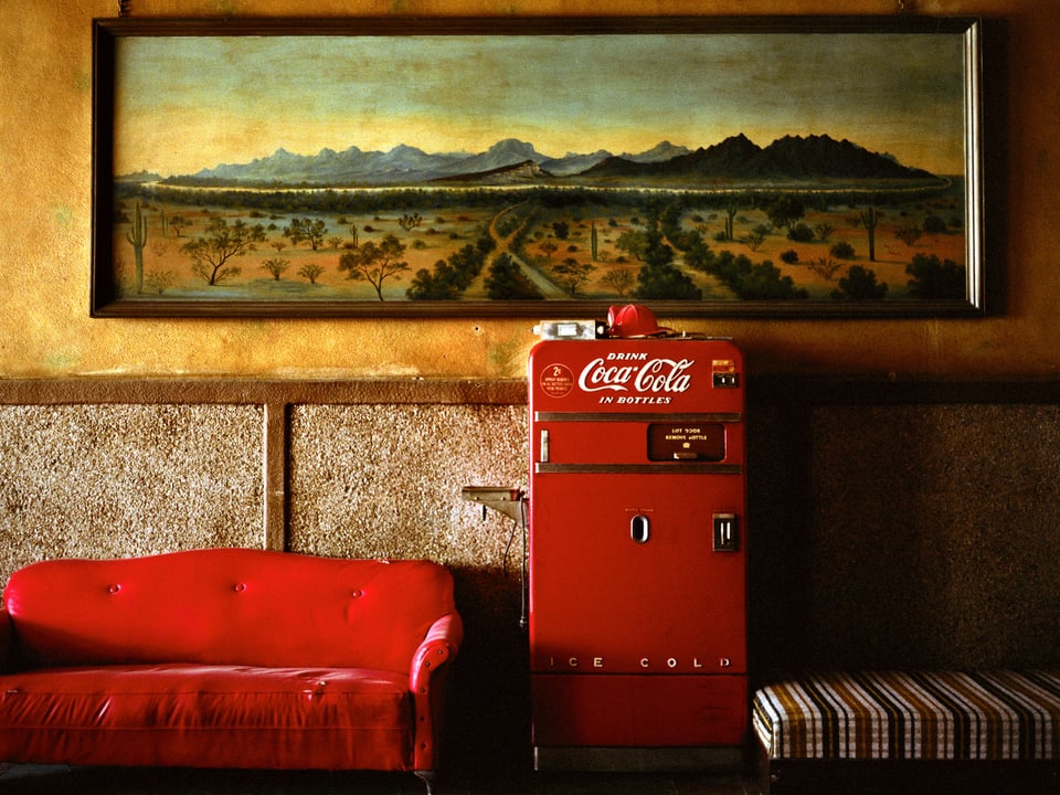 Links ein rotes Sofa, in der MItte ein roter Kühlschrank mit der Aufschrift Coca Cola.