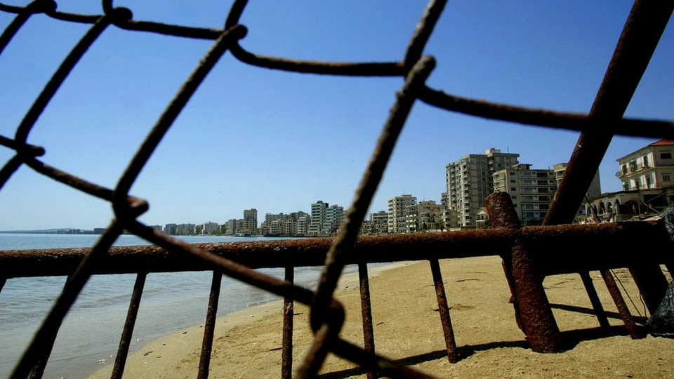 Stadt am Strand hinter Maschendrahtzaun.