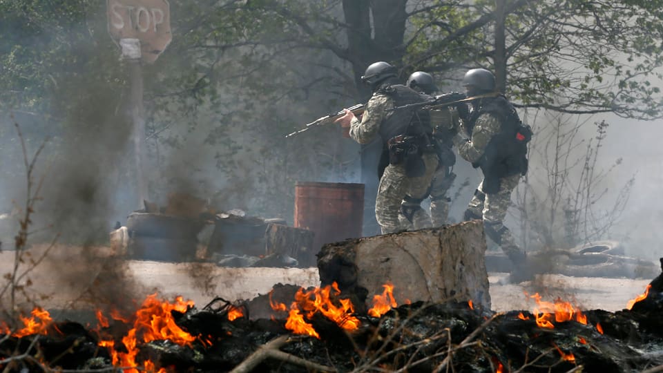 Bewaffnete Soldaten stehen vor brennenden Trümmern.