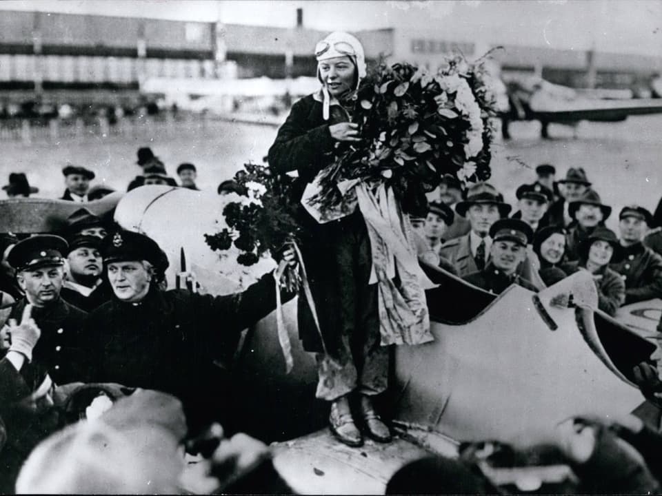 Schwarz-Weiss-Aufnahme von Elly Beinhorn mit Blumenstrauss auf einem Flugzeug