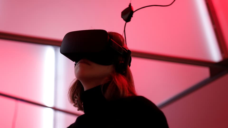 Eine Frau mit VR-Bitlle und Kabl in einem pink ausgeleuchteten Raum.