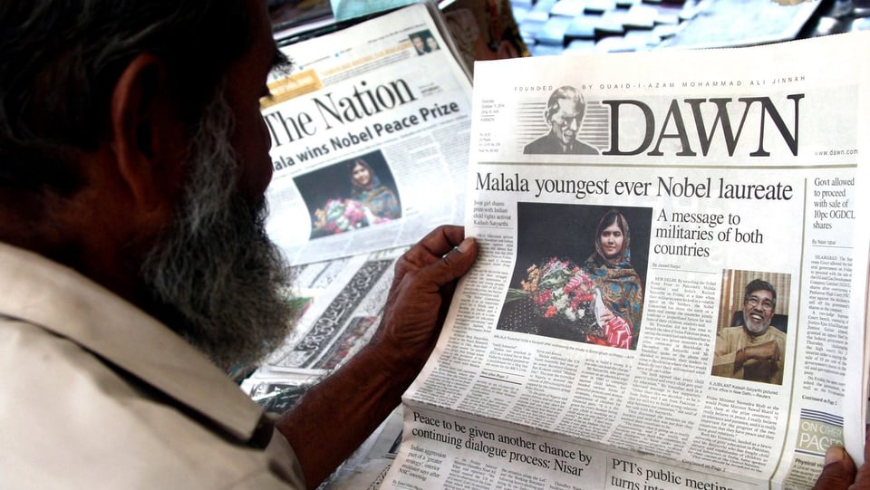 Ein Mann sieht sich die Titelseite einer Zeitung an, auf der ein Bild von Malala Yousafzai und ihrer Ehrung zu sehen ist. 