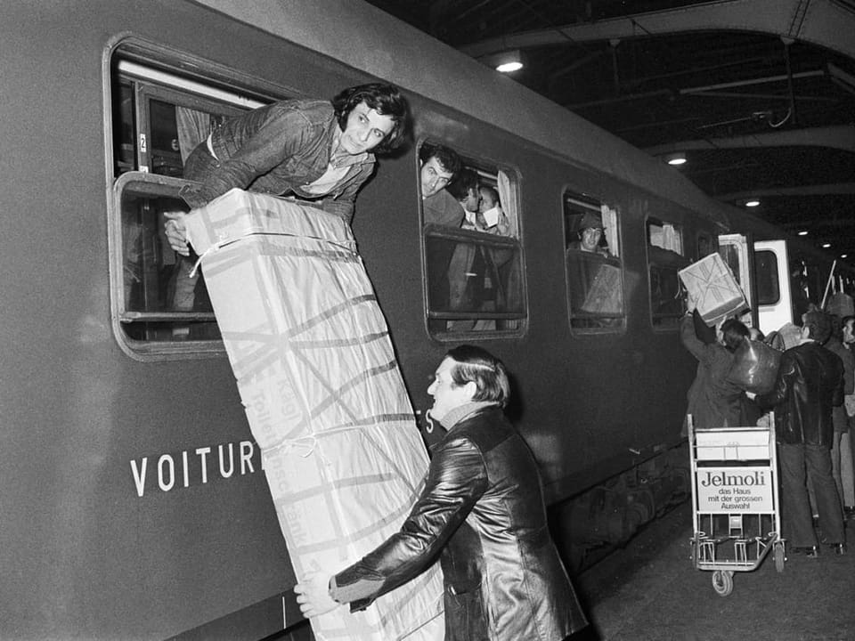 Ein Mann reicht einer Frau ein grosses Paket durch ein Zugfenster.