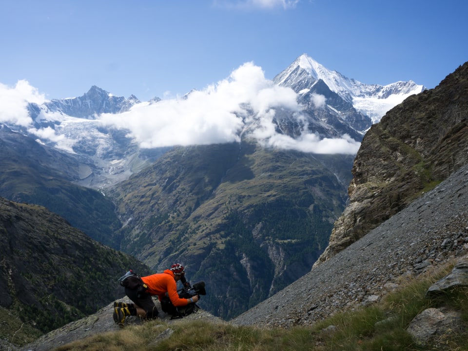 Kameramann filmt auf den Knien mit Bergkulisse im Hintergrund.