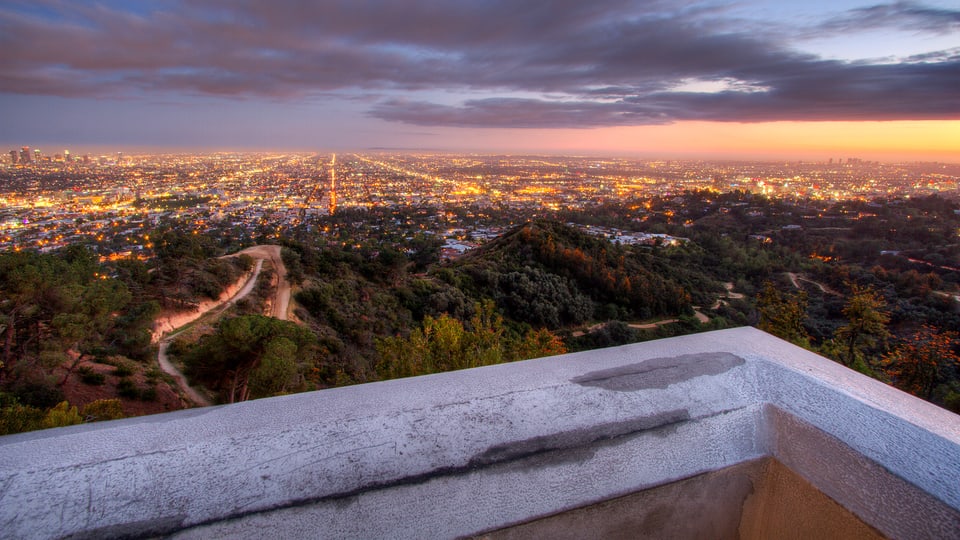 Blick von einem Balkon über die Millionenmetropole Los Angeles, deren Lichter in der Dämmerung schimmern.