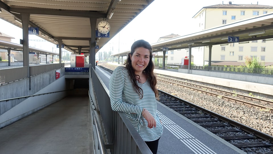 Junge Frau steht auf dem Perron am Bahnhof und lächelt freundlich in die Kamera