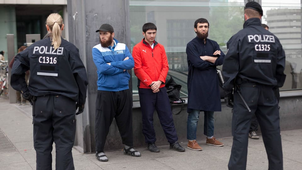 Drei Männer stehen einer Polizistin und einem Polizisten gegenüber