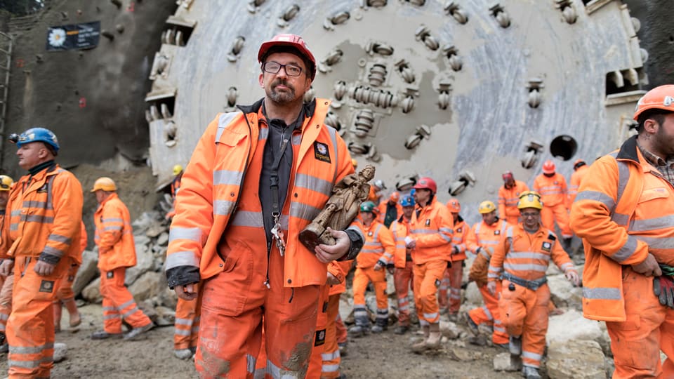 Bauarbeiter in orangen Kleidern vor einer Tunnelbohrmaschine.