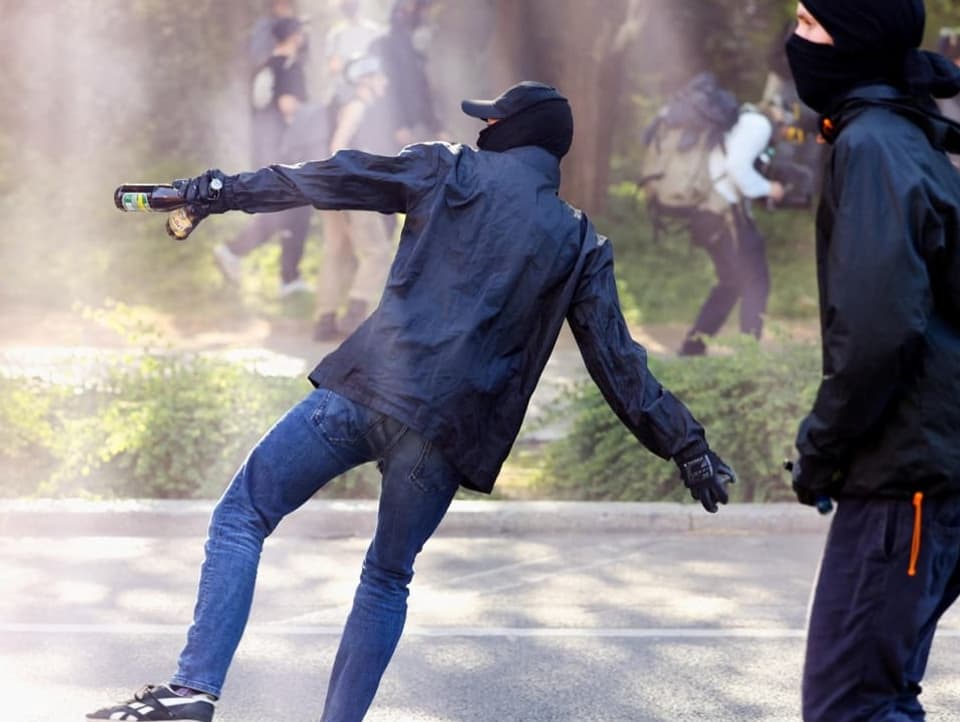 Zwei Personen rennen auf die Polizei zu; einer macht eine Wurfbewegung