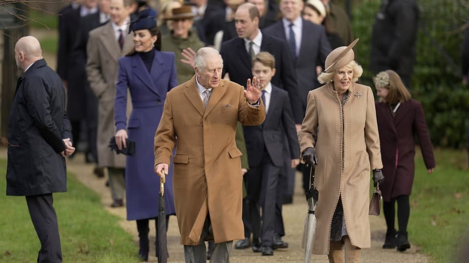 Feierlich angezogene royale Familie geht auf Schotterweg durch Tor.