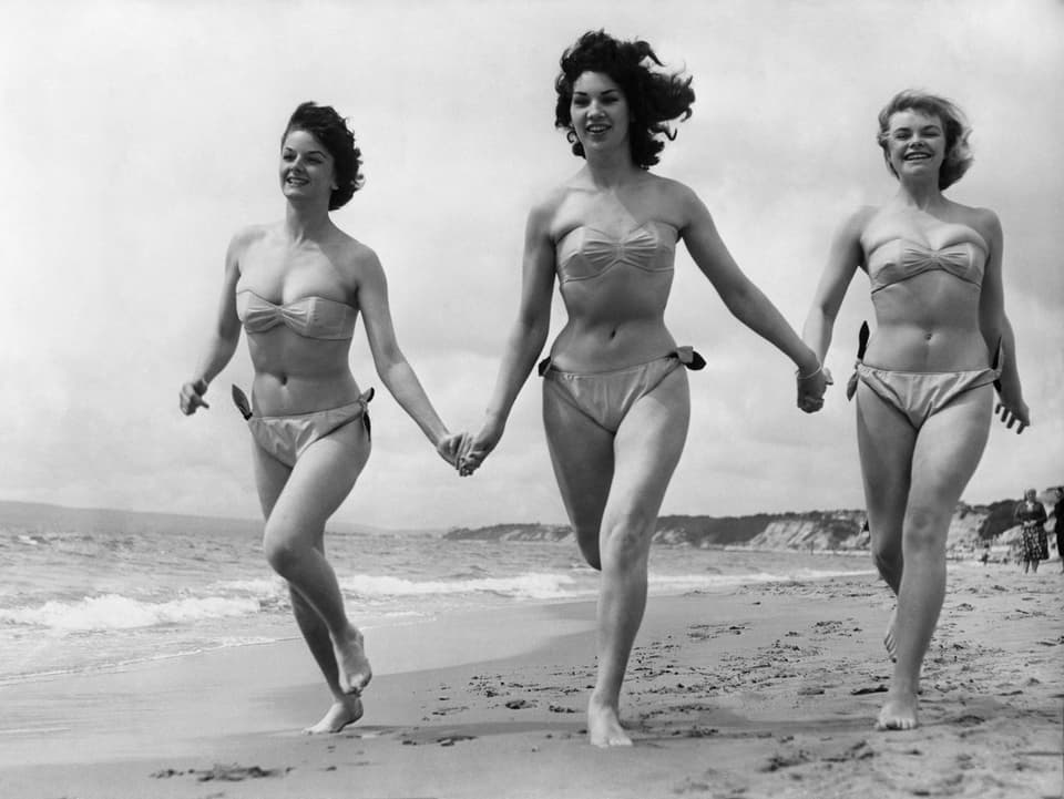 Drei junge Frauen im Bikini rennen über den Strand