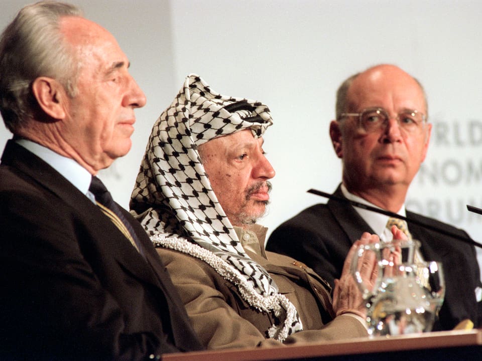 Beim WEF 1994 sitzt der damalige israelische Aussenminister Shimon Peres (links) an einem Tisch mit Palästinenserführer Jassir Afafat (Mitte). Hinten: WEF-Gründer Klaus Schwab. 
