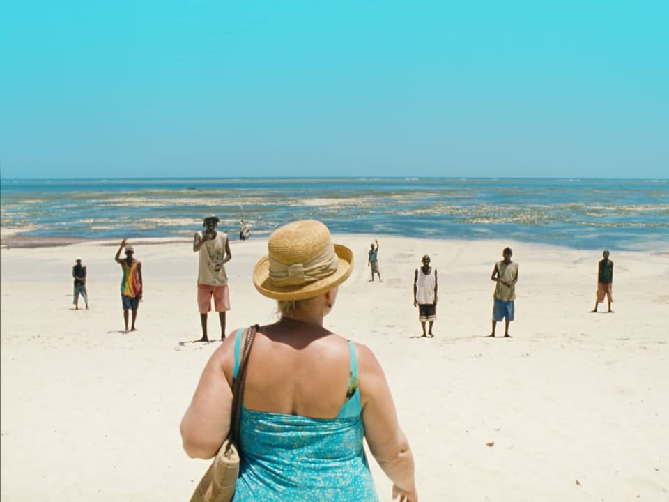 White old woman standing on the beach where many black men seem to be waiting for her