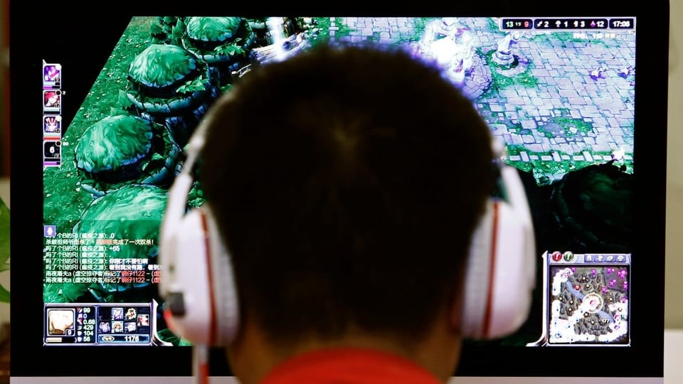 Männliche Person sitzt mit Kopfhörern vor einem Onlinegame.