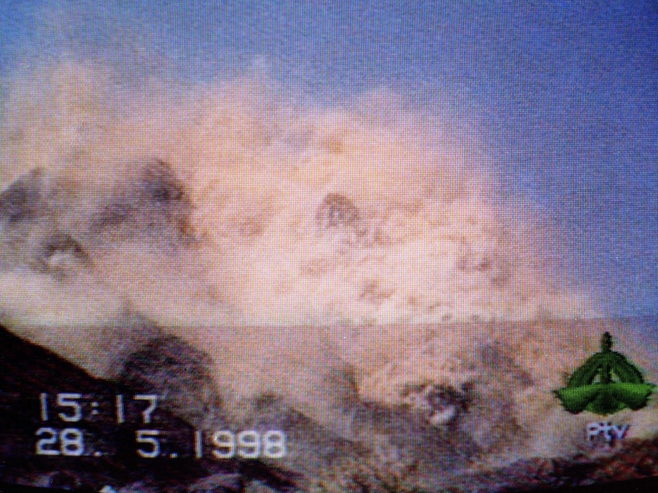 Videostill von einer Berglandschaft, aus der nach einem Atomtest eine Staubwolke aufsteigt.