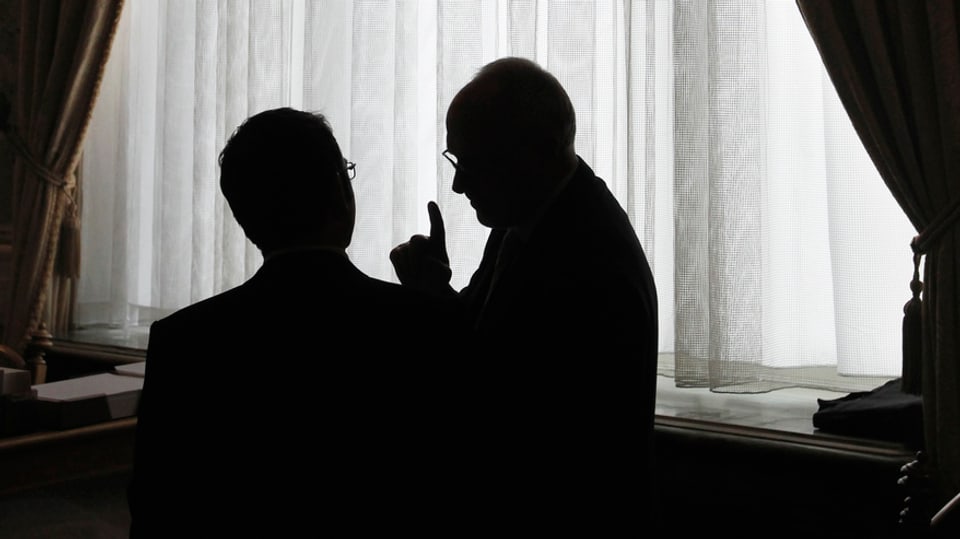 Silouhette zweier Männer im Bundeshaus im Gespräch vor einem Fenster mit weissem Vorhang