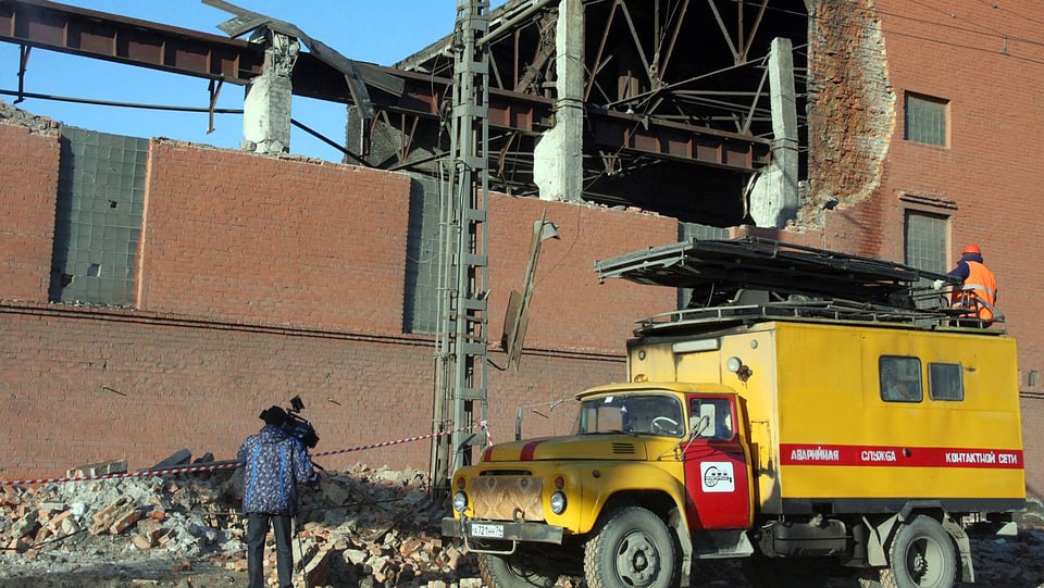 Gelber Lastwagen vor eingestürztem Gebäude.