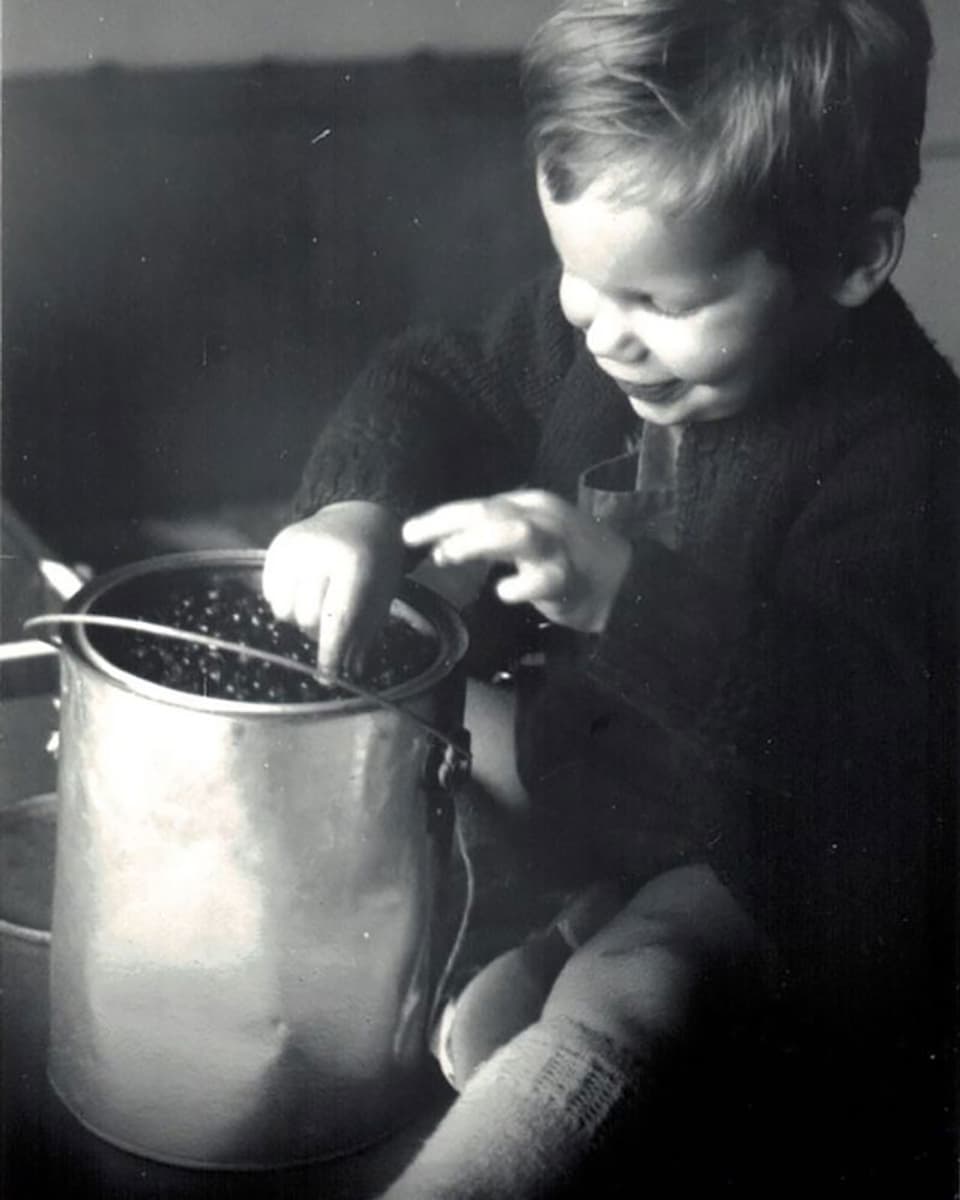 Ein kleines Kind isst Heidelbeeren aus einem Metalleimer.
