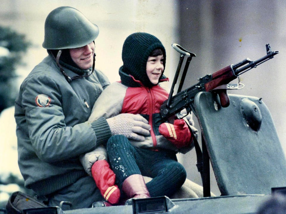 Soldat mit Kind auf Panzer sitzend, ein lächelndes Kind auf dem Schoss haltend