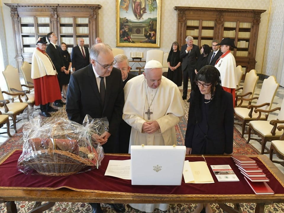 Guy Parmelin und der Papst begutachten Gaben auf einem Tisch.