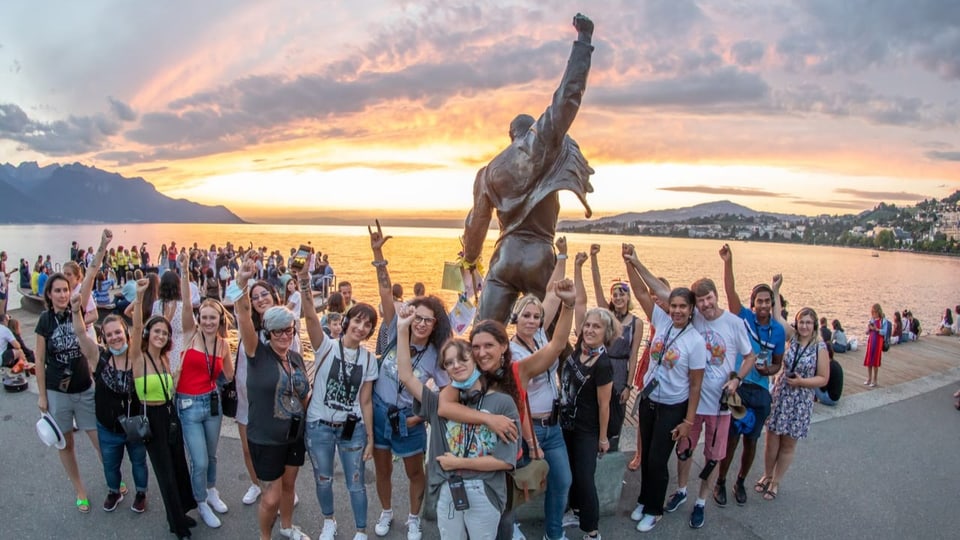 Viele Menschen stehen vor einer Statue und halten die Faust in die Luft. Im Hintergrund ist ein See zu sehen.