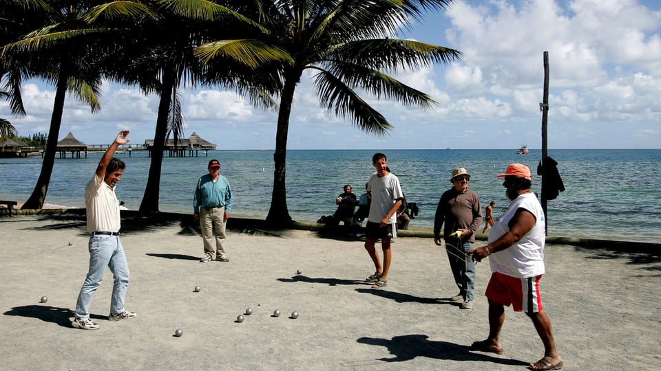 Fünf Männer spielen an einer Strandpromenade Pétanque.