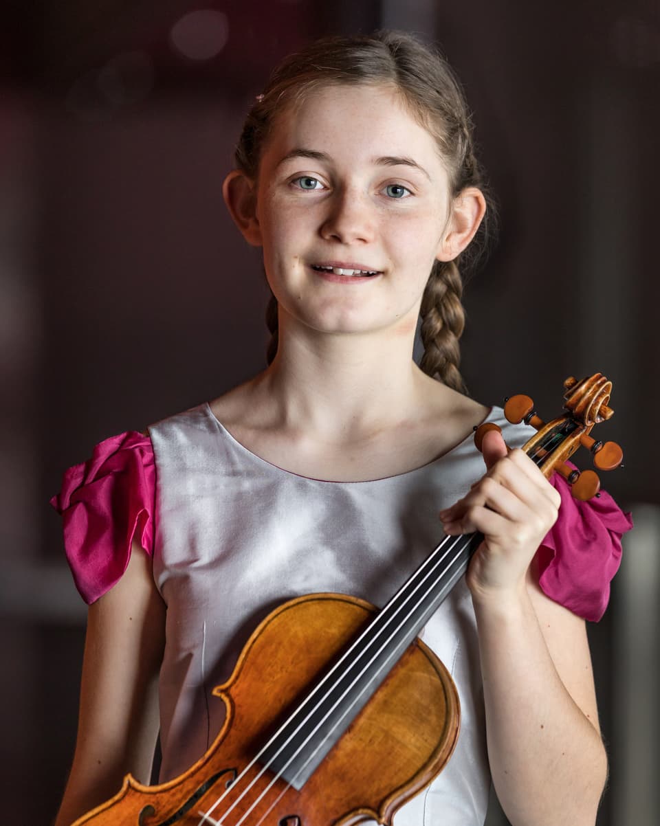 Ein Mädchen mit Zöpfen hält eine Geige in der Hand.