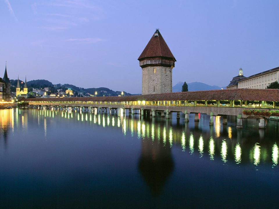 Zu sehen ist die Holzbrücke Kapellbrücke in Luzern in der Abenddämmerung.