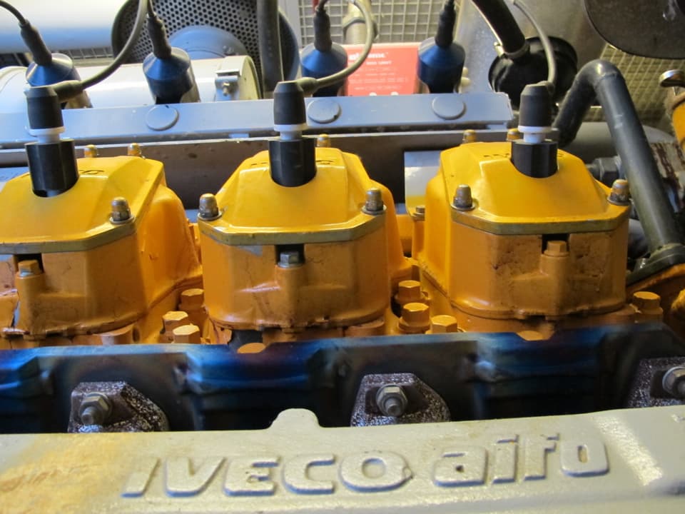 Gelber Motorenteil, davor die graue Aufschrift "Iveco".