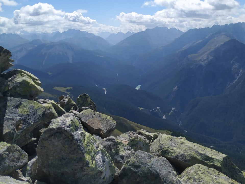 Steine im Vordergrund  mit einem Panorama in ein Tal im Engadin.