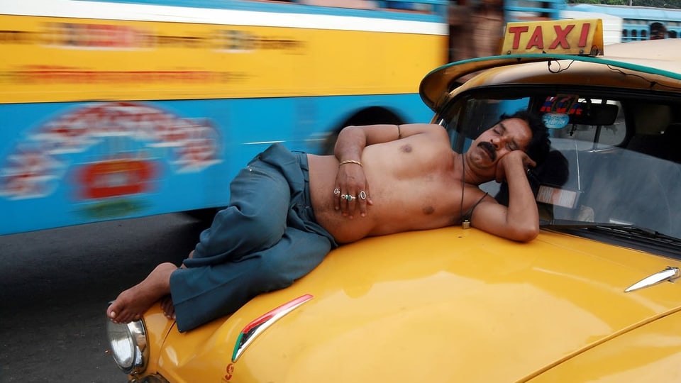 Taxifahrer schläft auf Kühlerhaube, Indien