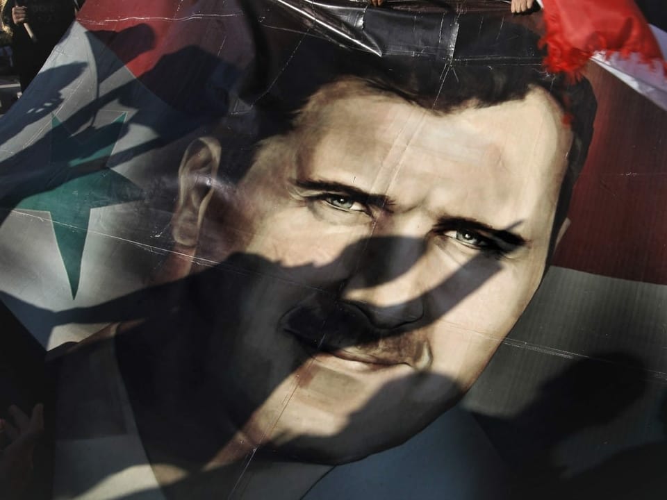 Die Schatten von Syrern fallen auf ein Riesenposter, das Präsident Baschar Assad während einer unterstützenden Kundgebung in Damaskus, Syrien, zeigt.