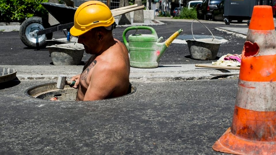 Ein Bauarbeiter arbeitet an einer Strasse. Im Vordergrund steht ein Warntöggel
