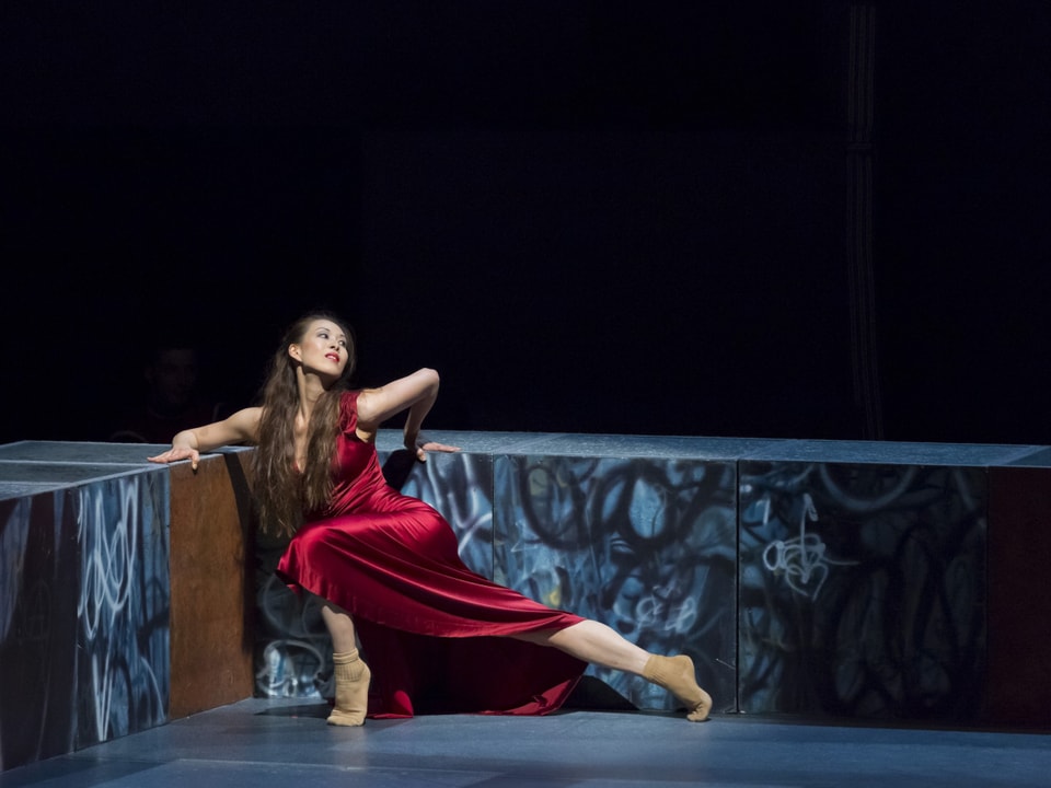Eine Tänzerin räckelt sich auf der Bühne, in einem roten Samtkleid.