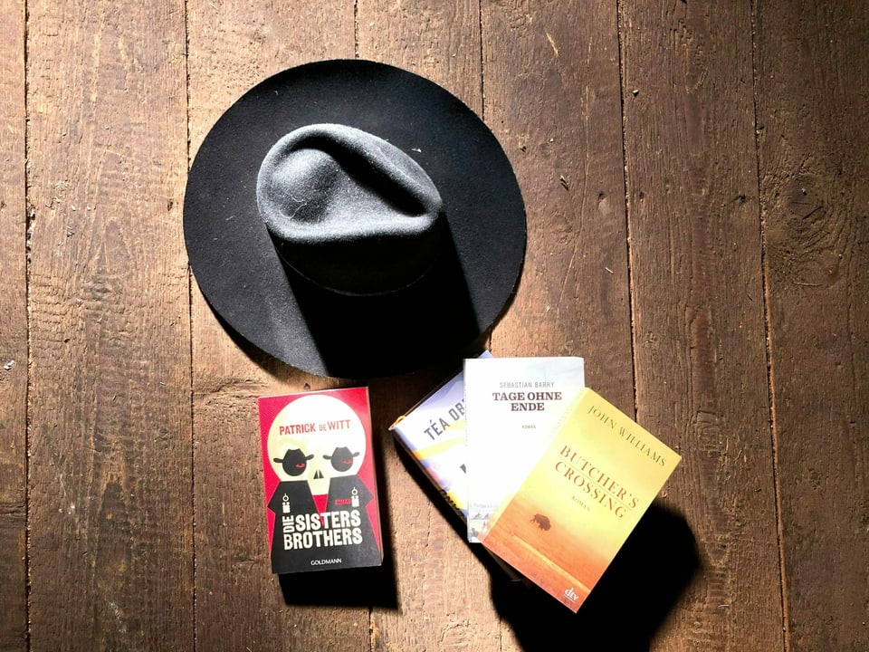 Cowboy-Hut und Western-Bücher auf einem dunklen Dielenboden.