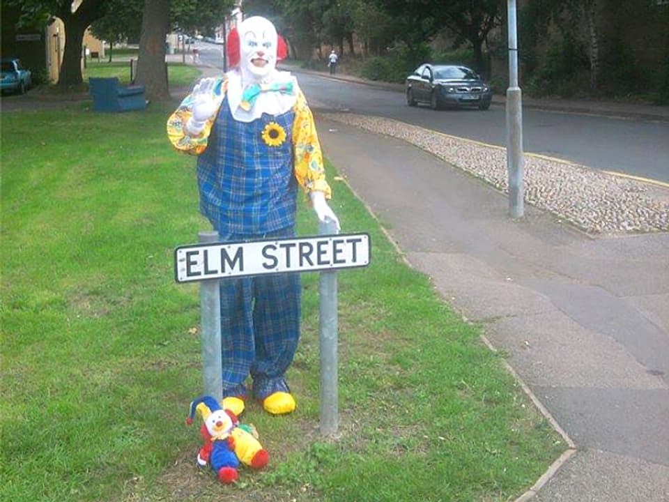 Clown hinter Strassenschild stehend