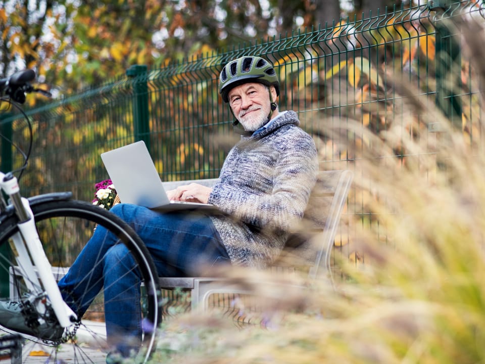 Mann mit E-Bike macht Rast auf einer Parkbank und studiert Reiseroute.