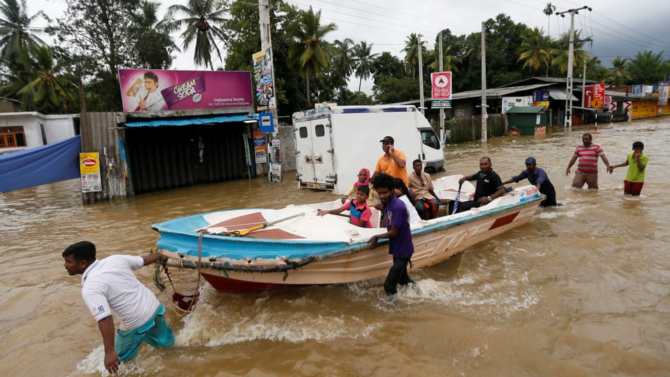 Menschen zeihen ein Ruderboot durch eine überschwemmte Strasse in einem Dorf