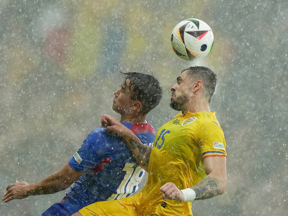 Two football players compete for a header in the rain.