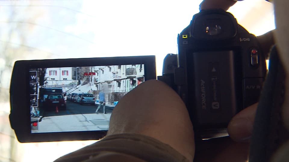 Ein Überwacher hält eine Digitalkamera in der Hand. Auf dem Monitor ist die überwachte Person sichtbar.