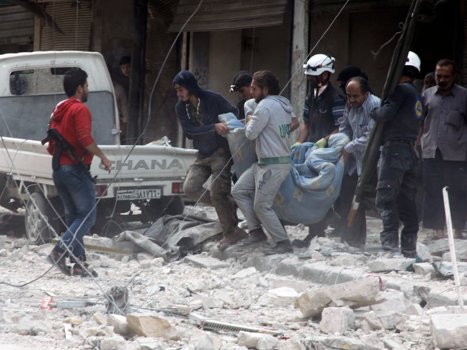 Männer tragen einen Leichensack durch Schutt in Aleppo