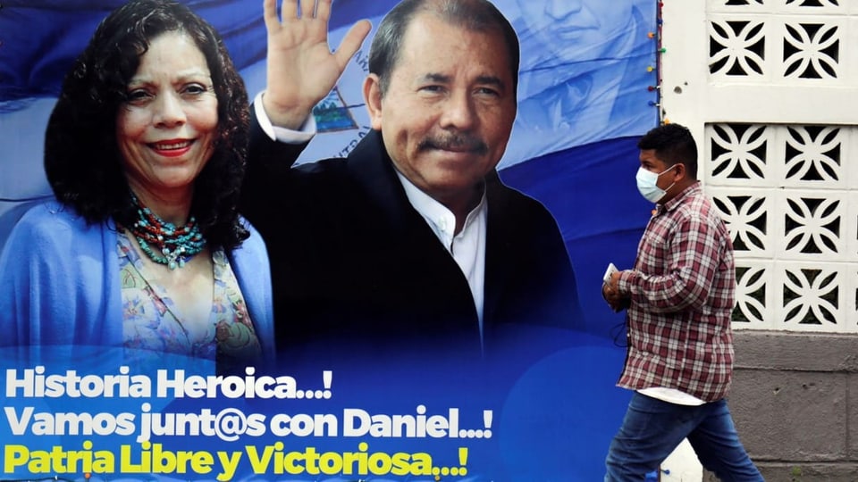 Mann läuft an Plakat vorbei. Darauf ist ein winkender Ortega und seine Frau abgebildet.