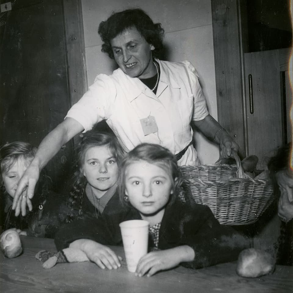 Eine Frau steht hinter Kindern, die an einem Tisch sitzen.